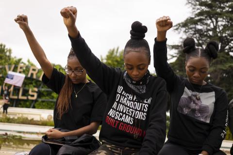 Photo by Aaron Guy Leroux of three young Black women with with fists up in the air