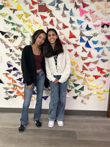 Youth activists Kaia and Lillian stand in front of their project “Butterfly Effect: Migration Is Beautiful” in the lobby at Cal Wellness’ Oakland, California, office. 