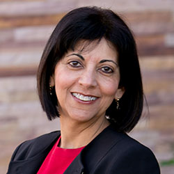 Shaheen Kassim-Lakha's headshot, a woman with black hair smiling wearing a red shirt and a black jacket.
