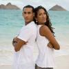 A Black woman and man standing back to back in front of a beach.