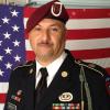Middle-aged, latino male in US Army uniform with a red beret in front of an American flag
