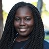 Black woman smiling with a dark blue shirt in front of trees.