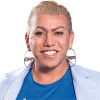 A picture of Bamby Salcedo with short blonde hair and hoop earrings. She is also smiling with a Blue grey blazer and a Blue shirt with The TransLatin@ Coalition logo.