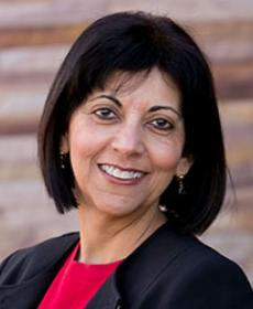 Shaheen Kassim-Lakha's headshot, a woman with black hair smiling wearing a red shirt and a black jacket.